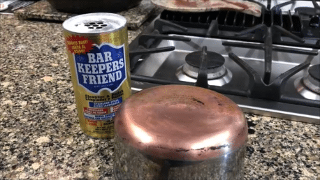 A can of copper spray next to a pot on a stove.