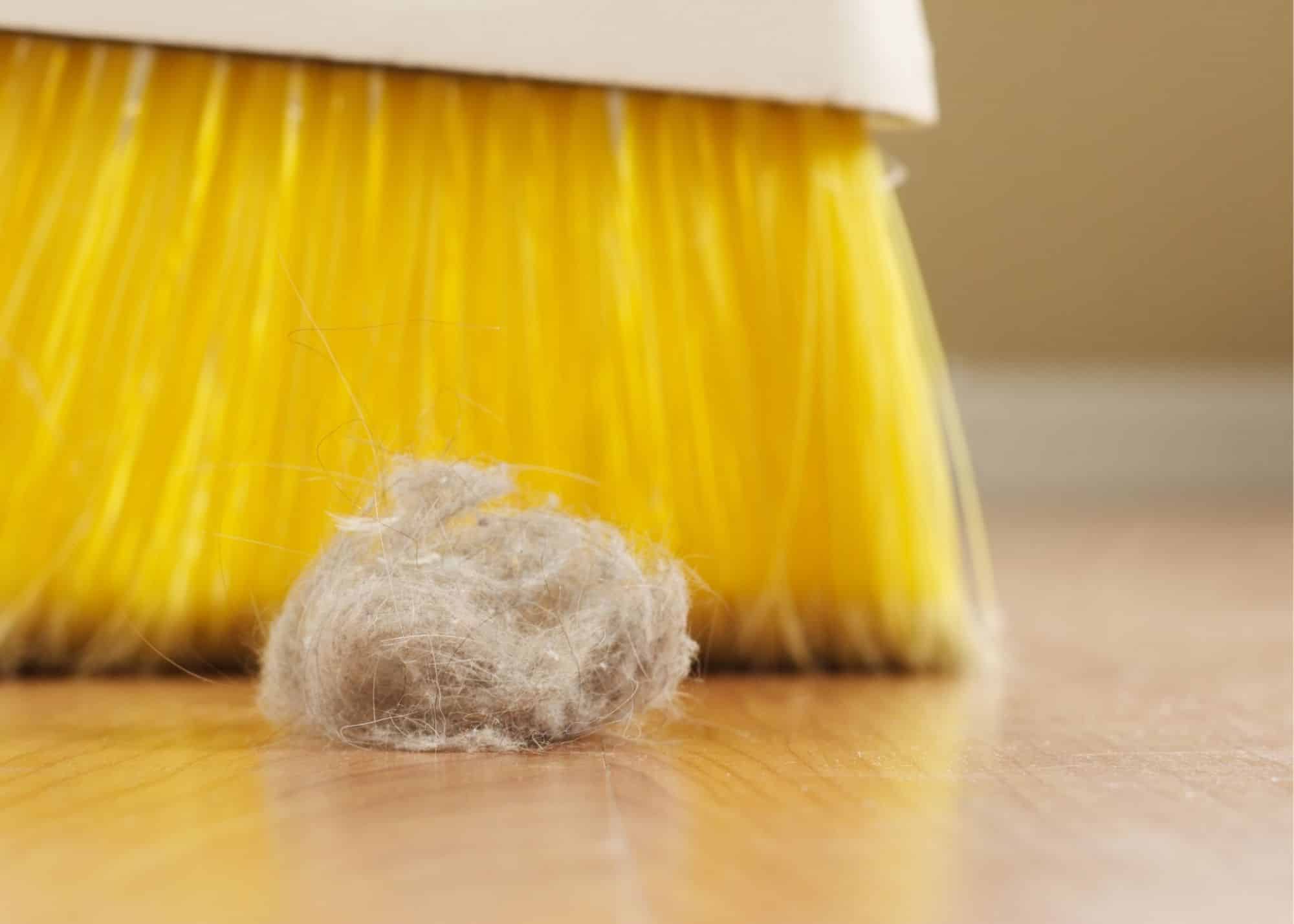 A yellow broom with a ball of wool on the floor.