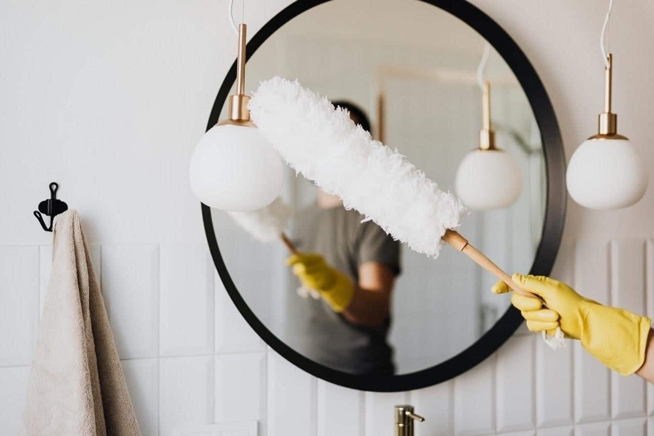 A woman performing move-in cleaning by sanitizing a bathroom mirror with a mop.