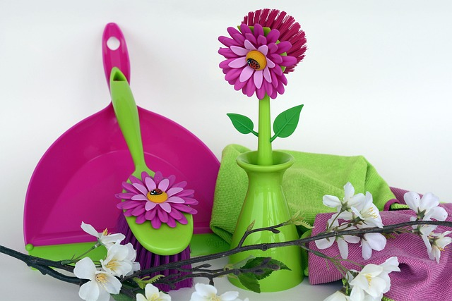 A pink and green vase with flowers and a pink and green broom.