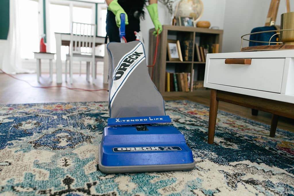 A woman performing house cleaning jobs by vacuuming a rug.