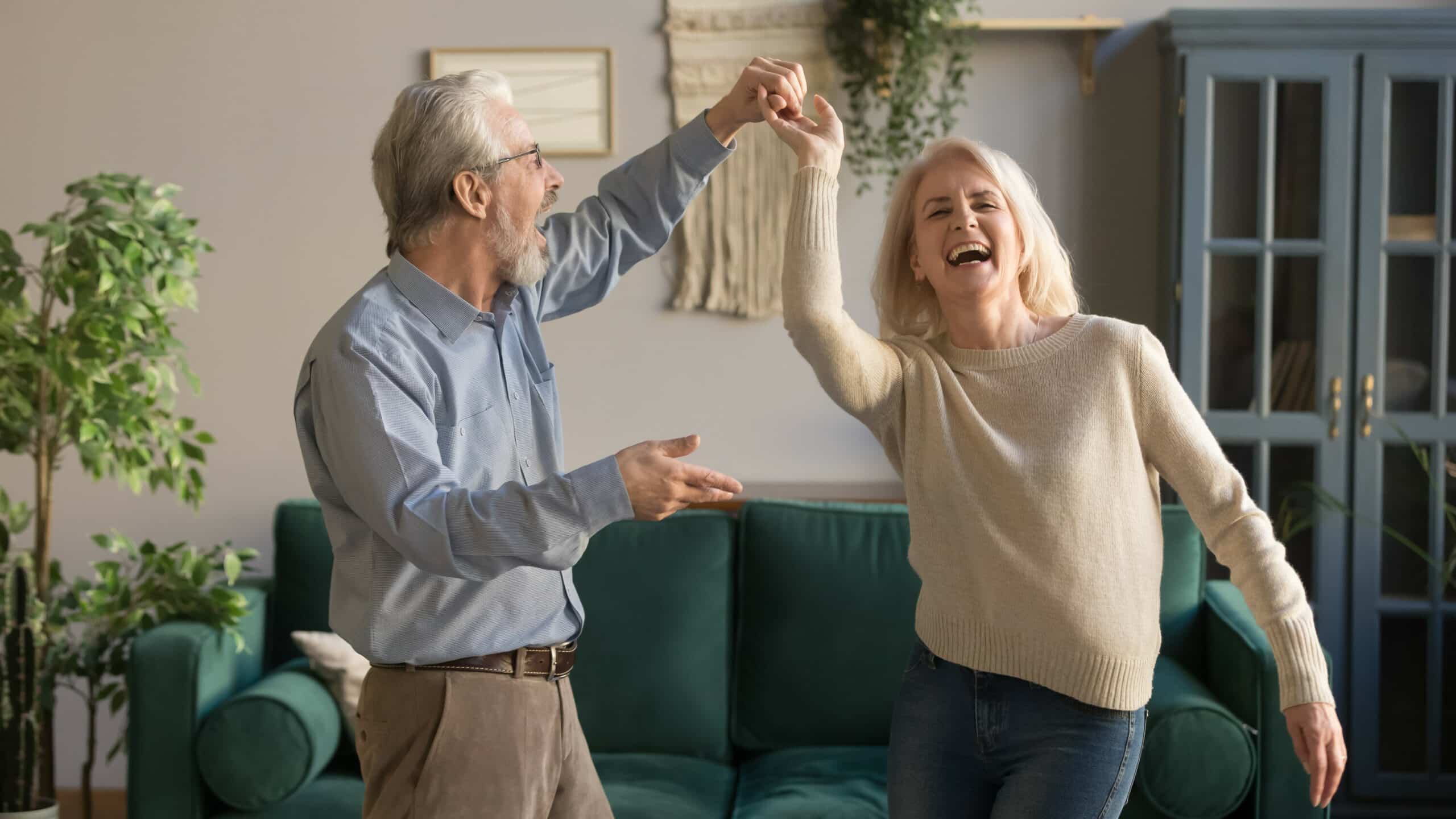 An older couple dancing in their living room, taking a joyful break from house cleaning.