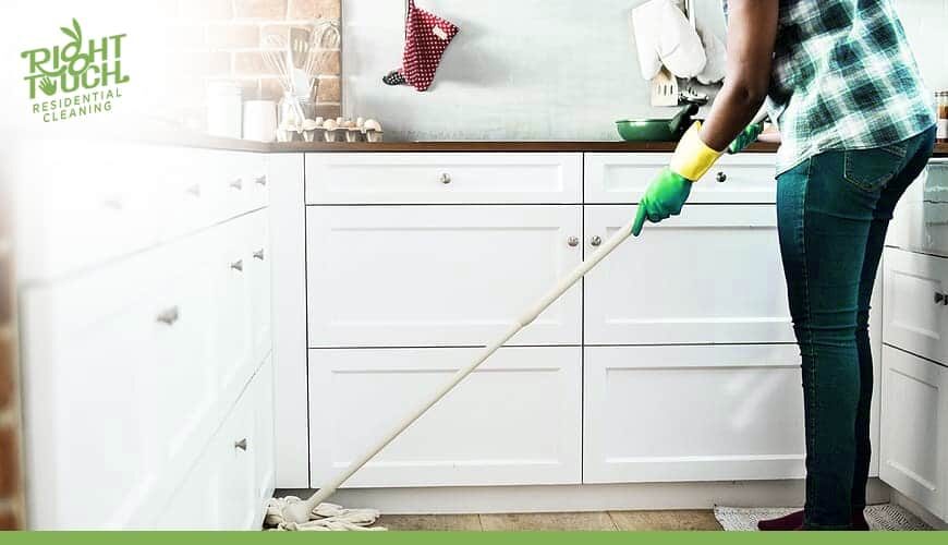A woman cleaning a kitchen with a mop.