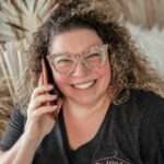 Headshot of smiling woman business owner talking on the phone with sparkly glasses.