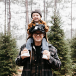 Father smiling happily with his young son on his shoulders walking in the forest.